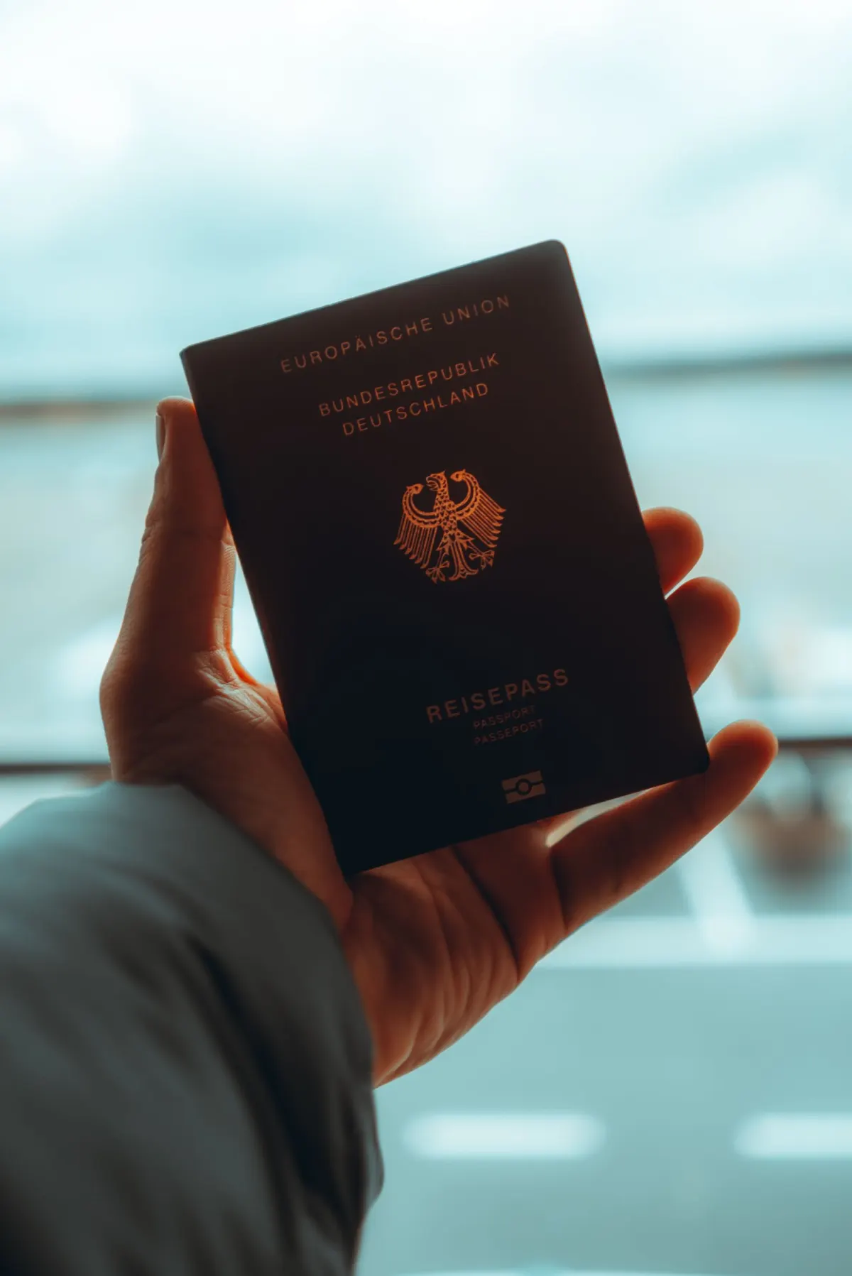 A hand holding a German passport up against a bright window.